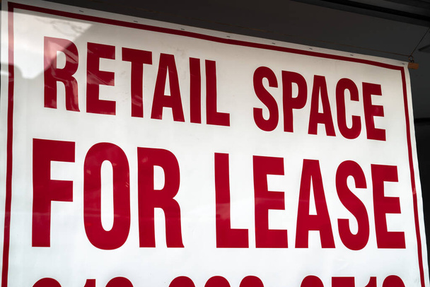 A red and white sign saying retail space for lease with border hangs in a vacant storefront glass window in Chicago during the COVID-19 or cornavirus outbreak and pandemic. - Photo, Image