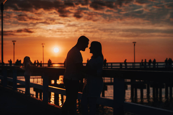 Portrait silhouette of a beautiful newlywed couple. A loving man hugs a girl at sunset, against the background of the sea standing on the pier. - Foto, immagini