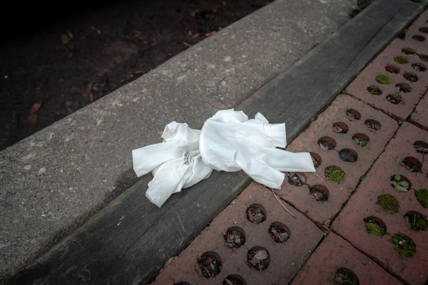 Используемые белые пластиковые, резиновые или латексные медицинские перчатки лежали частично наизнанку рядом с бордюром, засоряющим улицу в мусоре, используемом для защиты от COVID-19 или вспышки коронавируса и пандемии.
. - Фото, изображение