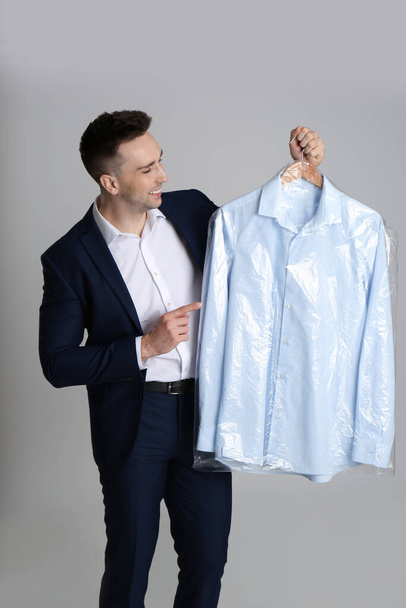 Man holding hanger with shirt in plastic bag on light grey background. Dry-cleaning service - Photo, image