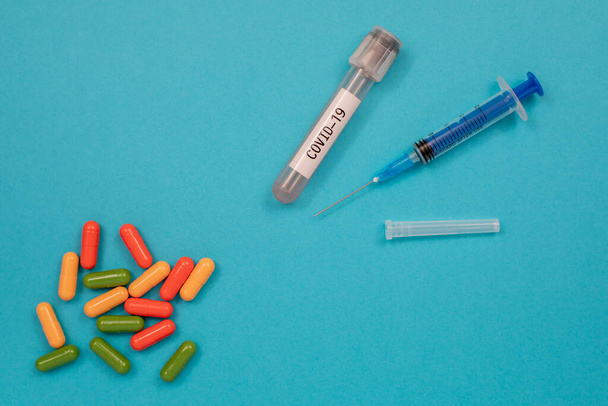 Multicolored tablets are scattered on the table, a syringe, a needle, a test tube. Top view with copy space, flat lay. - Photo, image