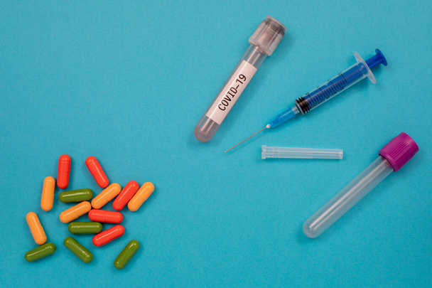 Multicolored tablets are scattered on the table, a syringe, a needle, a test tube. Top view with copy space, flat lay. - 写真・画像
