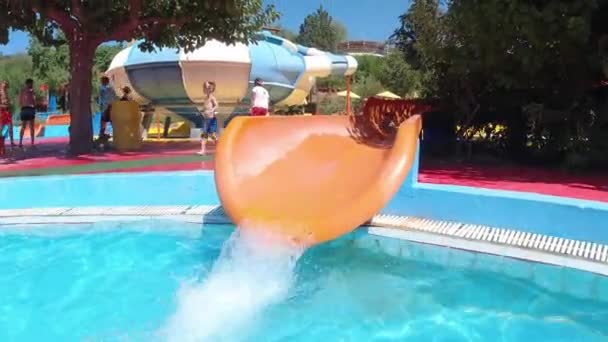 Niña feliz divirtiéndose con tobogán de agua en una piscina disfrutando de una excursión de un día a un parque de atracciones acuático durante las vacaciones familiares de verano
 - Metraje, vídeo