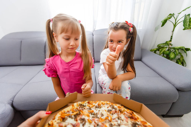 Dwie małe dziewczynki jedzące wielką pizzę w domu - Zdjęcie, obraz