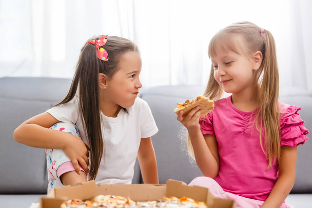 Two little girls eating huge pizza at home - Photo, Image