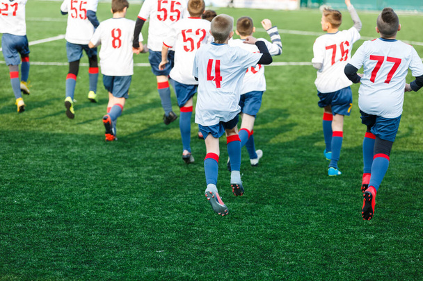 Chłopcy w białej czarnej odzieży sportowej biegający po boisku. Młodzi piłkarze dryblować i kopać piłkę nożną w grze. Szkolenia, aktywny tryb życia, sport, koncepcja aktywności dzieci - Zdjęcie, obraz