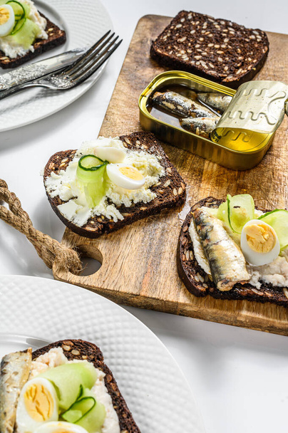 Heerlijke aperitieftapas, zachtgekookte eieren en broodjes sardines in blik. Salade met spinazie en gedroogde tomaten. Witte achtergrond. Bovenaanzicht. - Foto, afbeelding