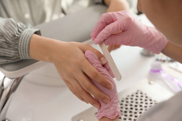 Professional manicurist filing client's nails in beauty salon, closeup - Φωτογραφία, εικόνα