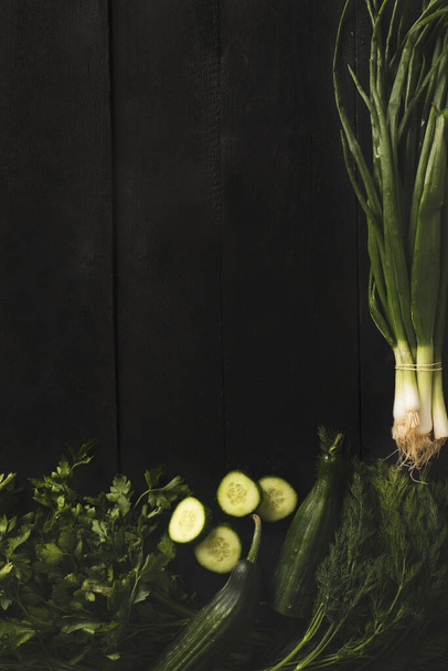 緑の新鮮な野菜、キュウリ、新鮮な玉ねぎ、小包と木の暗い背景にディル - 写真・画像