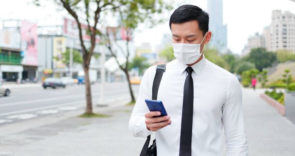 asian business man use smartphone while walking with face mask - Фото, изображение
