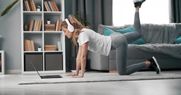 Girl doing exercises while watching tutorial on laptop - Felvétel, videó