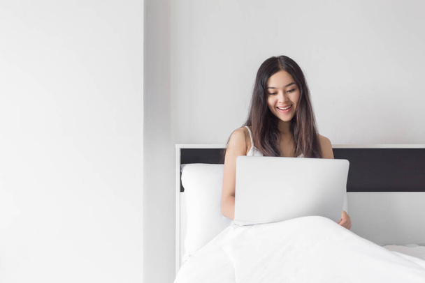 Jovem beleza feliz mulher asiática sentada na cama com computador portátil
. - Foto, Imagem