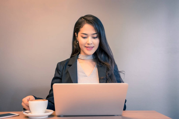 若い美しさアジアのビジネス女性がノートパソコンで作業し、コーヒーを飲む. - 写真・画像