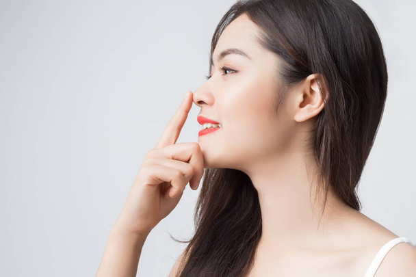 Fiatal gyönyörű ázsiai nő mosolygós arccal és piros ajkakkal az orrát érintve. - Fotó, kép