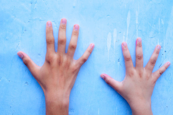 Two human hands one of male and another female over a blue colored background contrasting the size of two different individuals. - Foto, afbeelding