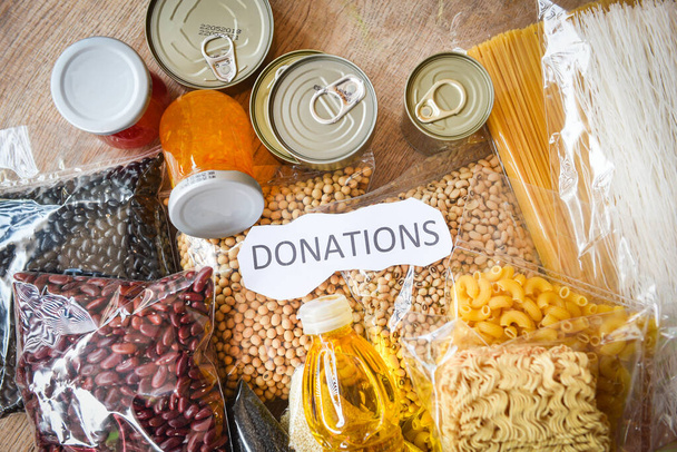 Donations food with canned food on wooden table background / pasta canned goods and dry food non perishable with pea beans cooking oil instant noodles macaroni , donate concept - Photo, Image
