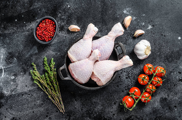 Ωμά μπούτια κοτόπουλου, πόδια με βότανα και μπαχαρικά σε ένα τηγάνι. Βιολογικό κρέας πουλερικών. Μαύρο φόντο. Άνω όψη. - Φωτογραφία, εικόνα