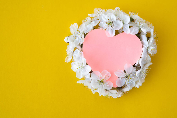 Cherry flowers on a yellow background, top view, flat layout. The concept of spring, summer, a sheet of paper in the form of a heart. Mother's Day, holidays, March 8th. - Photo, Image