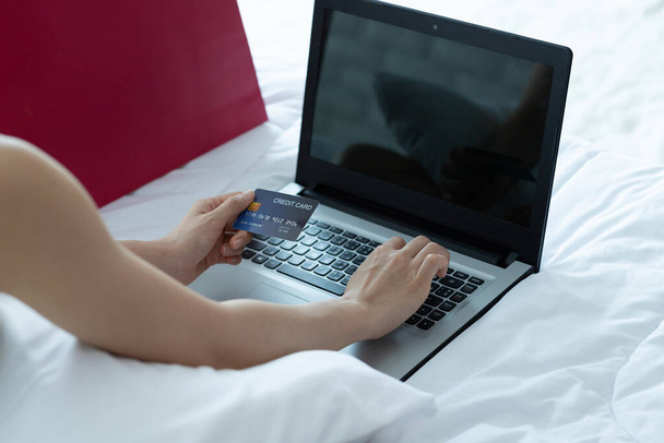Ázsiai nő online fizet. Vásárló online vásárlás hitelkártyával és laptoppal az ágyon otthon.shopping online koncepció. - Fotó, kép