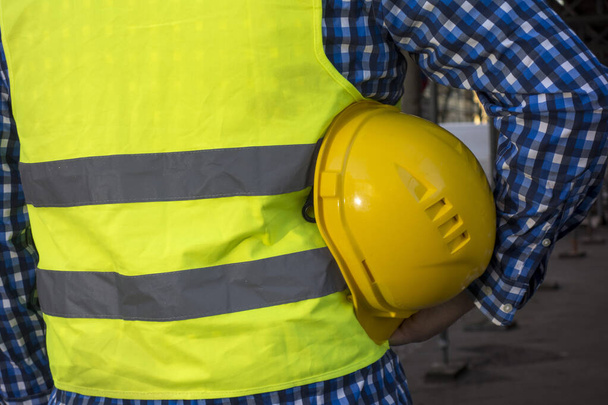 Imagen recortada de un trabajador de la construcción usando un chaleco de seguridad amarillo y manteniendo un casco amarillo en la axila
 - Foto, imagen