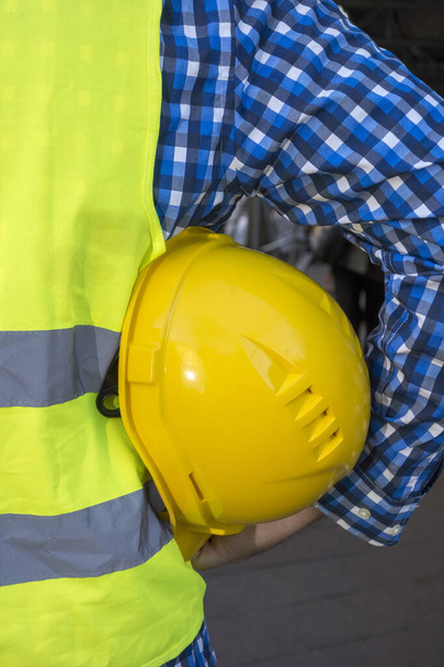 Imagen recortada de un trabajador de la construcción usando un chaleco de seguridad amarillo y manteniendo un casco amarillo en la axila
 - Foto, imagen