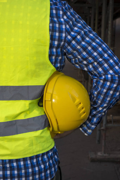 Image recadrée d'un ouvrier de la construction portant un gilet de sécurité jaune et gardant un casque jaune sous les bras
 - Photo, image