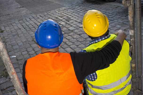 Back turned construction worker sitting and putting his hand on a colleague's shoulder - Photo, Image