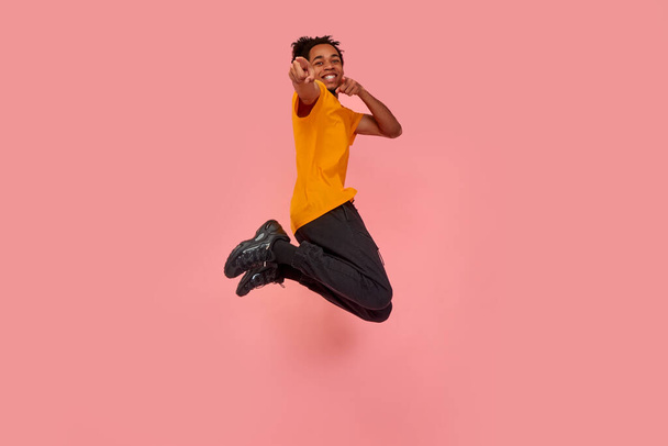 Full length shot of young surprised dark skinned man jumping in the air and pointing, choosing something, isolated on pink studio background. Freedom of choices, inspiration, human emotions concept - Fotoğraf, Görsel