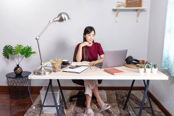A young, beautiful relaxing business asian girl use a laptop working remotely from home on desk as a freelancer, quarantine for Coronavirus and smart working concept - Photo, Image