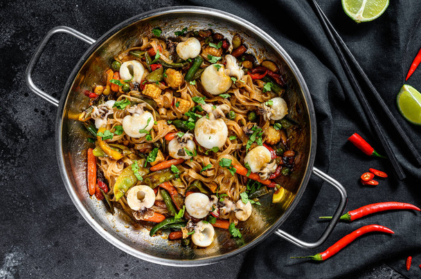 Stir fry noodles with seafood and vegetables in a wok pan. Black background. Top view. - Фото, изображение