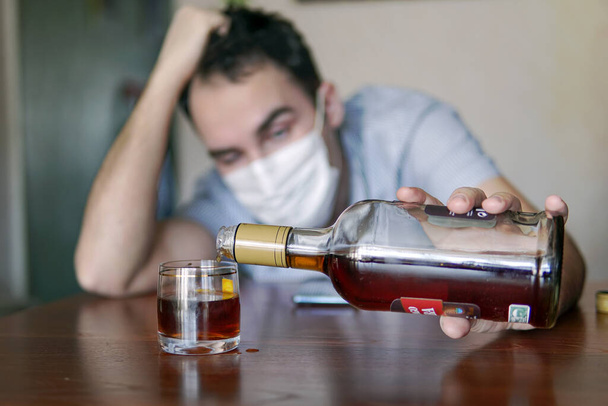 alkoholizmus, alkoholfüggőség és az emberek fogalma - férfi alkoholista egy üveg rummal otthon. Az unalomból egyedül berúgott munkanélküli specialistát karanténba zárják.. - Fotó, kép