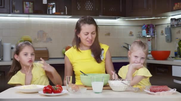 Mamma e le sue due figlie si divertono in cucina. Mamma insegna ai bambini a fare la pizza. Mamma felice e bambini felici stanno cucinando la cena insieme in cucina
. - Filmati, video