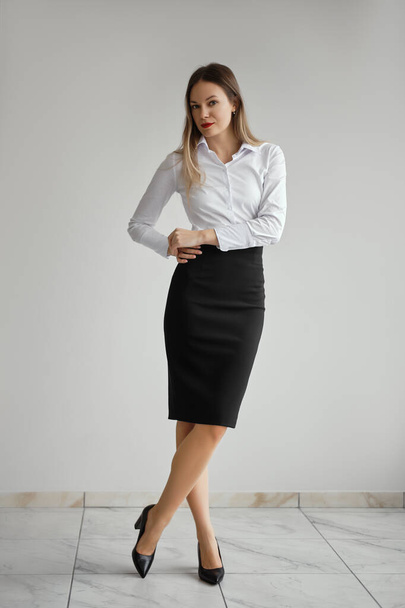 Slim girl in white shirt and black tight skirt posing near the wall - Photo, image