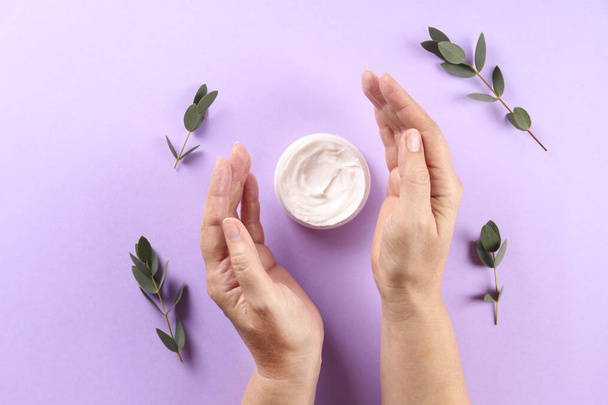 Revitalizing hand cream for healing and recovery after excessive use of soap and disinfectants. Adult woman applying moisturizing lotion. Copy space, close up, background, flat lay, top view. - Foto, Imagen