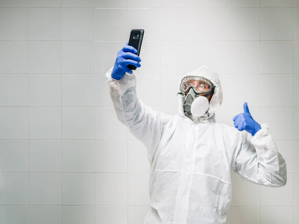 wetenschapper met beschermende apparatuur neemt een selfie met de mobiele telefoon. witte achtergrond - Foto, afbeelding