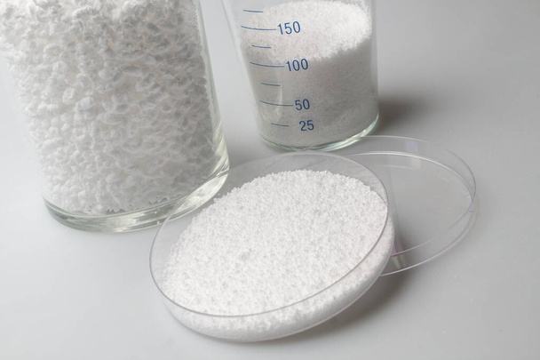 γυάλινο εργαστηριακό βάζο με δείγματα από χαλαρό λευκό συνθετικό καουτσούκ σε λευκό φόντο - Φωτογραφία, εικόνα
