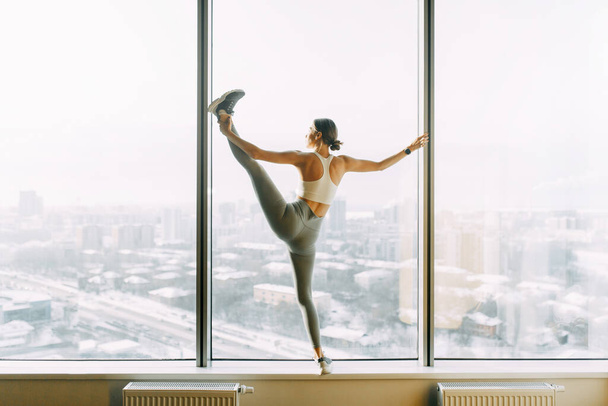  Stretching in the white room by the window. Beautiful girl athlete on the Mat. Flexibility exercises on a light background. - Fotografie, Obrázek
