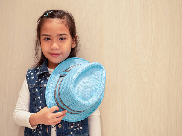 La niña sonreía y sostenía el sombrero azul en su mano con fondo de madera
 - Foto, imagen