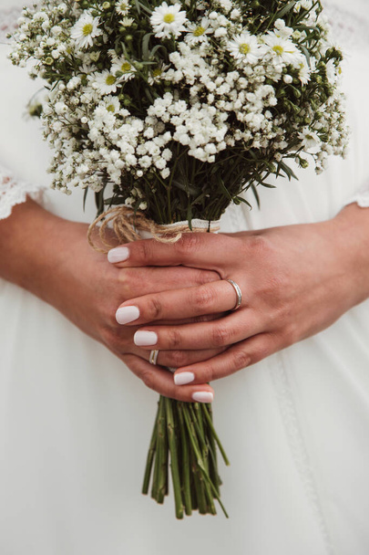 Novia en un vestido elegante. Hermoso ramo de bodas con flores blancas. Hermosa manicura. Anillo de boda. Espacio para texto
 - Foto, imagen