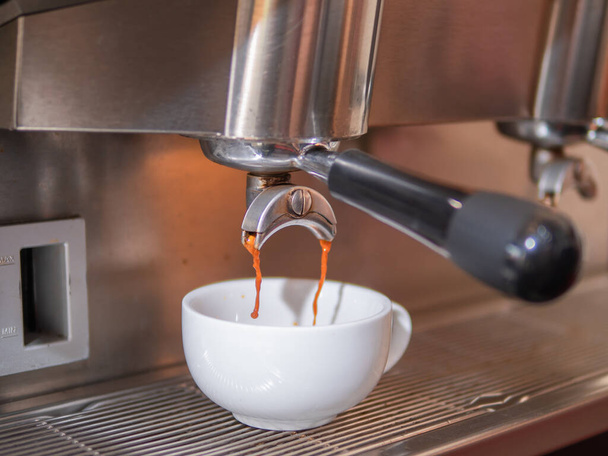 Świeża kawa wlewająca się z portafiltra ekspresu do białego ceramicznego kubka. Robi gorącą kawę z ekspresem do kawy. - Zdjęcie, obraz