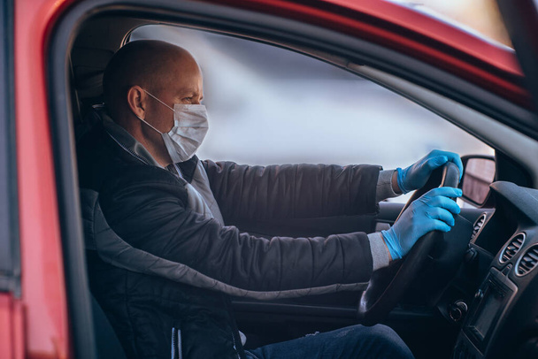 Ένας άντρας που οδηγεί αυτοκίνητο με προστατευτική ιατρική μάσκα και γάντια. Ασφαλής οδήγηση σε ένα ταξί κατά τη διάρκεια μιας πανδημίας coronavirus. Προστατέψτε τον οδηγό και τους επιβάτες από βακτήρια και μολύνσεις από ιούς σε καραντίνα - Φωτογραφία, εικόνα