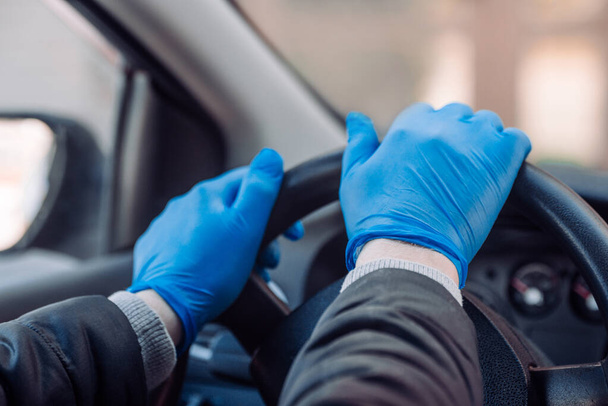 A man holds the steering wheel of a car in protective medical gloves. Hands close-up. Safe drive in a taxi during pandemic coronavirus. Protect driver and passengers from bacteria and virus infection - Foto, Bild