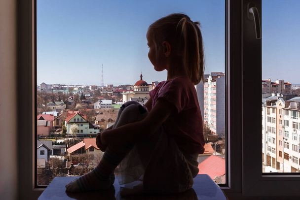 Silueta malé holčičky dívající se z okna na pozadí okna. - Fotografie, Obrázek