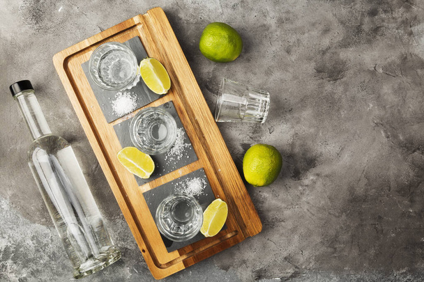 Tequila bottle and shots, limes, salt on wooden board. Top view, copy space - Fotó, kép