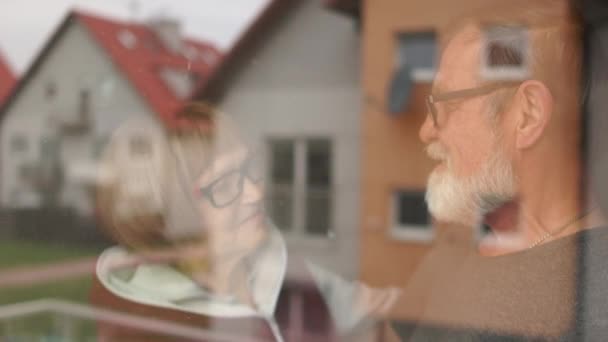 Elderly during quarantine coronovirus covid-19. Risk group. Husband and wife senior citizens dance behind glass near a window in their house - Materiał filmowy, wideo
