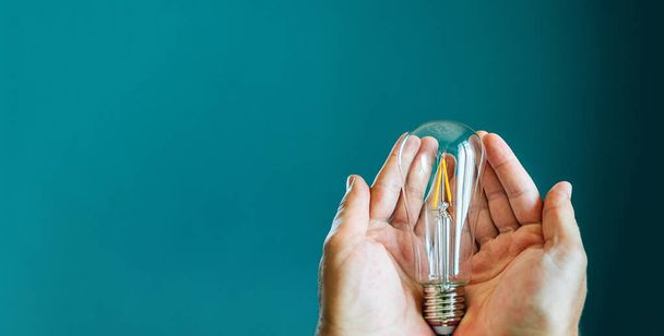 Two hands holding a light bulb on a green background with copy space - 写真・画像