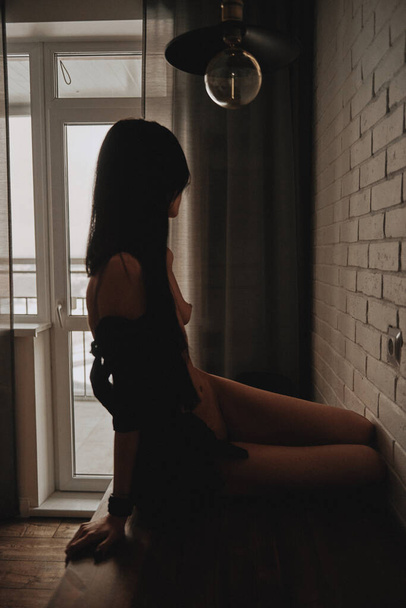 beautiful girl sitting on a table in a black shirt nude - Fotó, kép