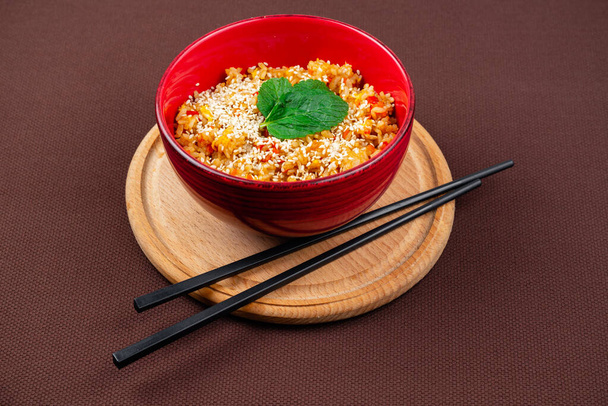 Κινέζικο ρύζι με σουσάμι, δυόσμο και μαύρο ξύλινο ρύζι chopsticks σε κόκκινο πιάτο σε ξύλινο στρογγυλό ταμπλό σε καφέ φόντο - Φωτογραφία, εικόνα