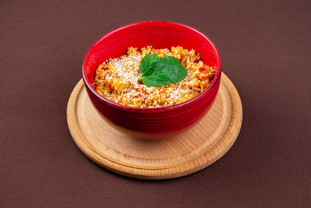 Riso cinese con semi di sesamo e menta in un piatto rosso su tavola rotonda di legno su fondo marrone
 - Foto, immagini