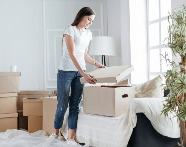 young woman opening a box in a new apartment - Foto, afbeelding
